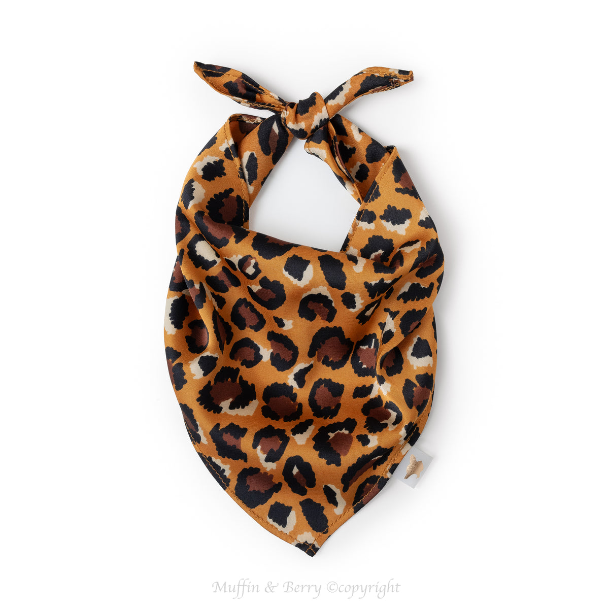 A leopard print pet bandana ROBIN with a tied top, featuring a pattern of black and brown spots on a warm orange-brown background, shown on a plain white background, by Muffin & Berry