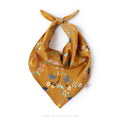 A gold mustard pet bandana with a colorful floral pattern, tied in a loop at the top, shown on a plain white background, by Muffin & Berry