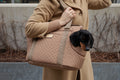 Woman walking outdoors carrying AMELIA camel quilted dog carrier bag on her shoulder, Dachshund peeking out of front opening, by Muffin & Berry